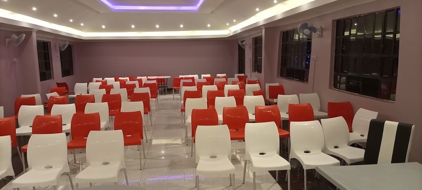 A conference room with rows of white and red chairs, large windows, and ceiling lights.