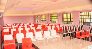A conference room with rows of chairs, large windows, and a logo on the wall. - Hope Cottages and Recreation Centre (Marigat)