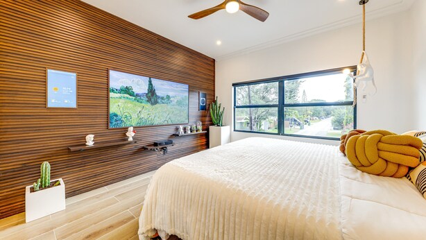 Un dormitorio con una cama grande, pared de paneles de madera, ventilador de techo, televisor, ventana y una planta.