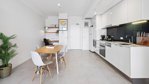 Een moderne keuken met witte kasten, een houten eettafel en een potplant.