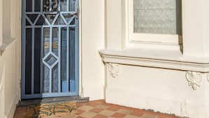 Entrada de un edificio con una reja metálica decorativa, un pequeño ventanal con persiana calada y suelo de baldosas.