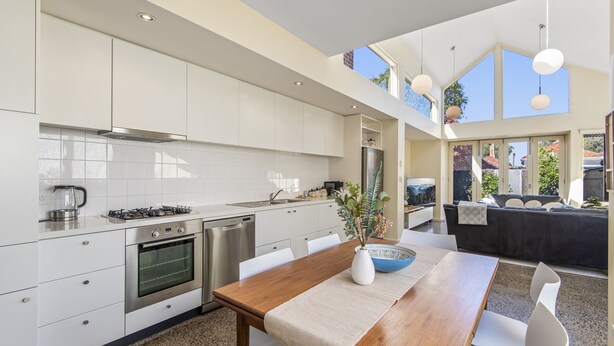 Una cocina moderna con armarios blancos, electrodomésticos de acero inoxidable y un comedor con mesa y sillas de madera.