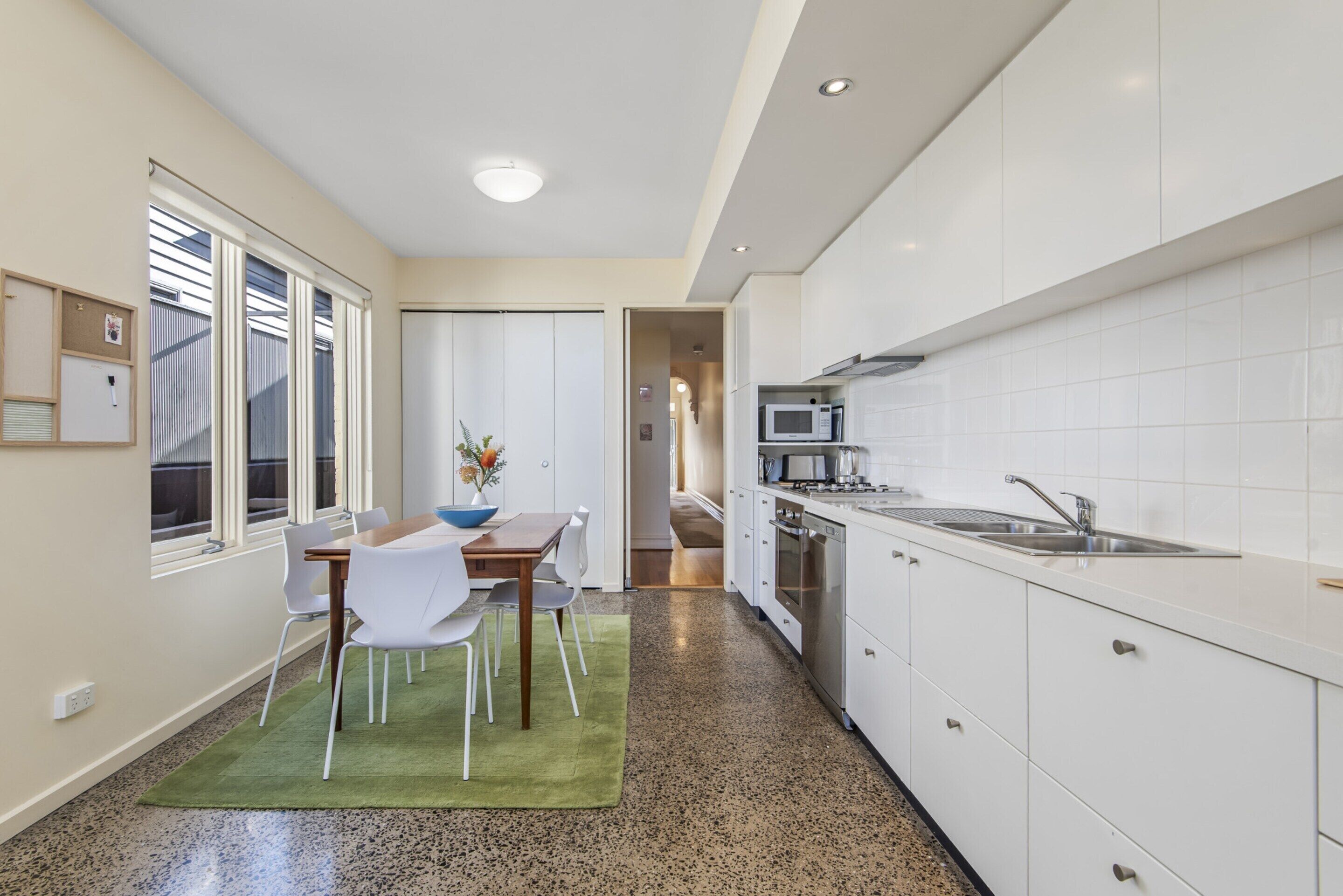 Una cocina moderna con armarios blancos, un microondas y un lavamanos. Hay una zona de comedor con una mesa y sillas.