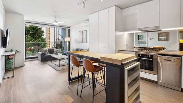 A modern kitchen with a central island, bar stools, and built-in appliances. - Cosy 2-bed With Pool, Bbq Area and Secure Parking (Brisbane)