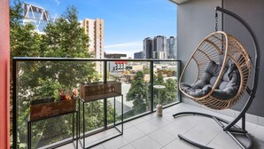 A balcony with a hanging chair, a small table, and a wicker basket. - Cosy 2-bed With Pool, Bbq Area and Secure Parking (Brisbane)