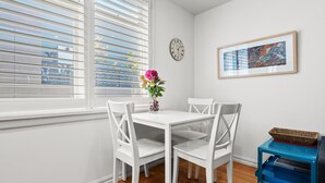 A white dining table with four chairs, a vase with flowers, a clock, and a framed abstract painting on the wall. - Convenient Apartment in Heart of Carlton (Melbourne)