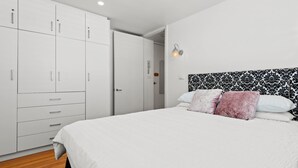 A bedroom with a large bed, white wardrobe, and a patterned headboard. - Convenient Apartment in Heart of Carlton (Melbourne)