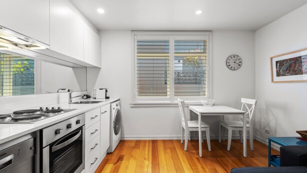 A compact kitchen with white cabinetry, a built-in oven, a washing machine, and a dining area with a table and chairs. - Convenient Apartment in Heart of Carlton (Melbourne)