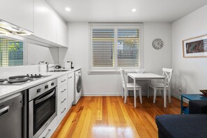 Uma cozinha compacta com armários brancos, forno embutido, máquina de lavar e área de jantar com mesa e cadeiras.