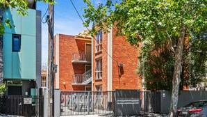 A multi-story brick building with a balcony on the second floor, a gated entrance, and a parked car. - Convenient Apartment in Heart of Carlton (Melbourne)