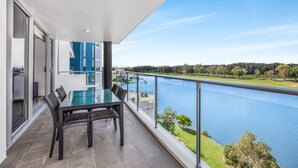 A balcony with a dining table and chairs, overlooking a lake and a golf course. - Lakeside Family Oasis With Pool, Gym and Balcony (Gold Coast)