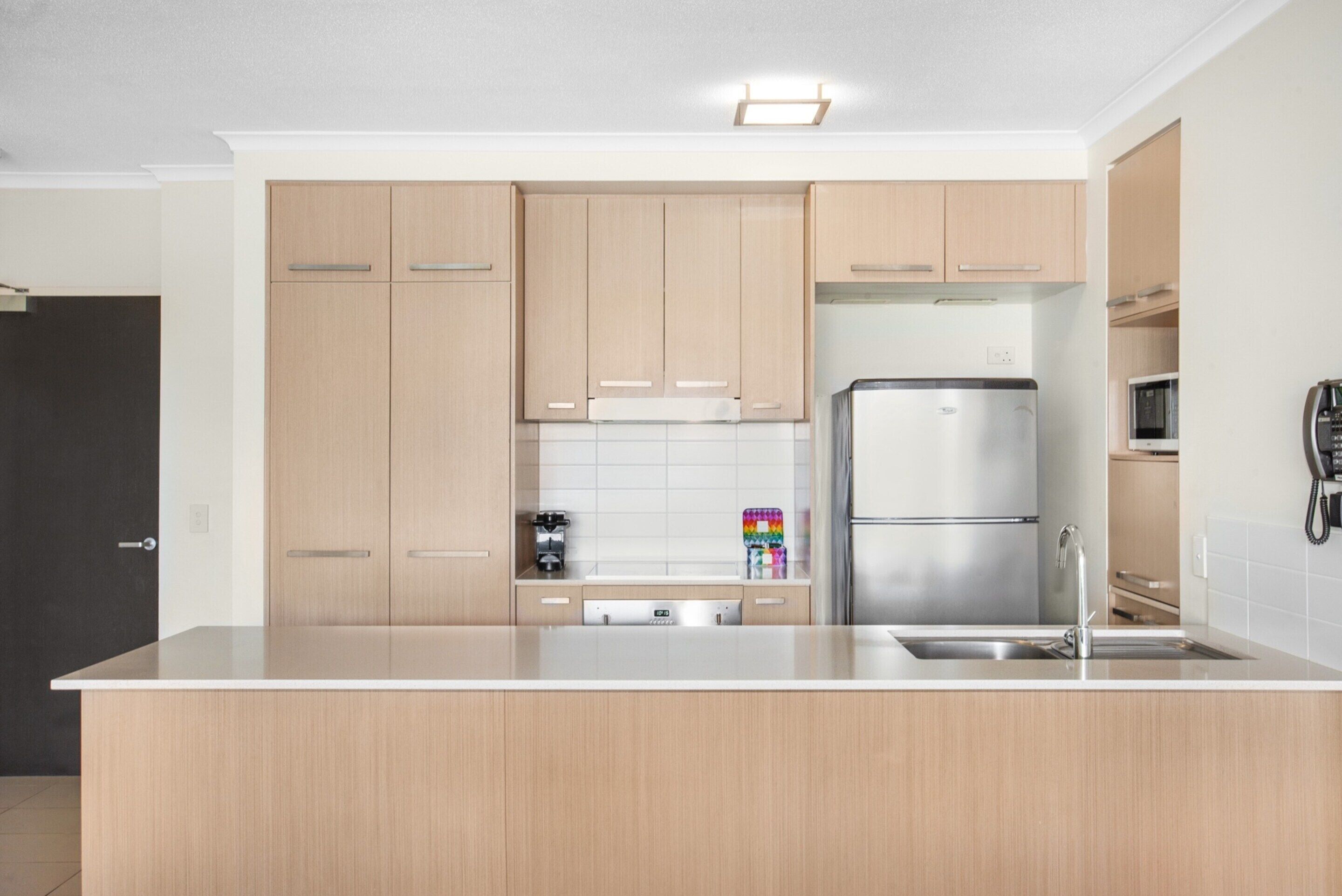 A modern kitchen with light wood cabinets, a stainless steel refrigerator, and a built-in dishwasher.