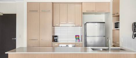 A modern kitchen with light wood cabinets, a stainless steel refrigerator, and a built-in dishwasher.