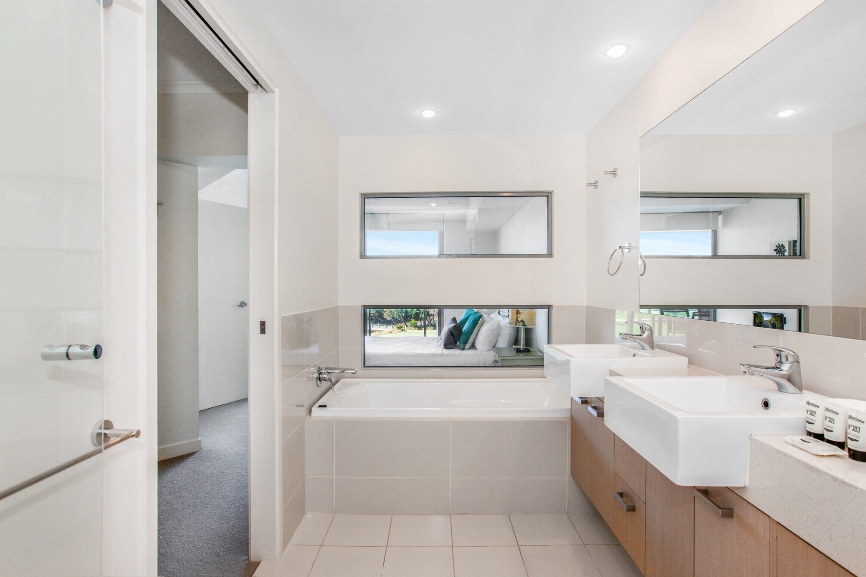 A modern bathroom with a large bathtub, two sinks, and a large mirror above the sinks.