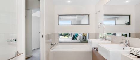 A modern bathroom with a large bathtub, two sinks, and a large mirror above the sinks.
