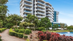 A multi-story hotel with balconies, surrounded by well-maintained gardens and a small pond. - Lakeside Family Oasis With Pool, Gym and Balcony (Gold Coast)