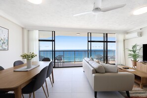 A modern living room with a balcony overlooking the sea, a dining area, and a TV on the right. - Beachfront Stylish Apartment With Ocean Views (Gold Coast)