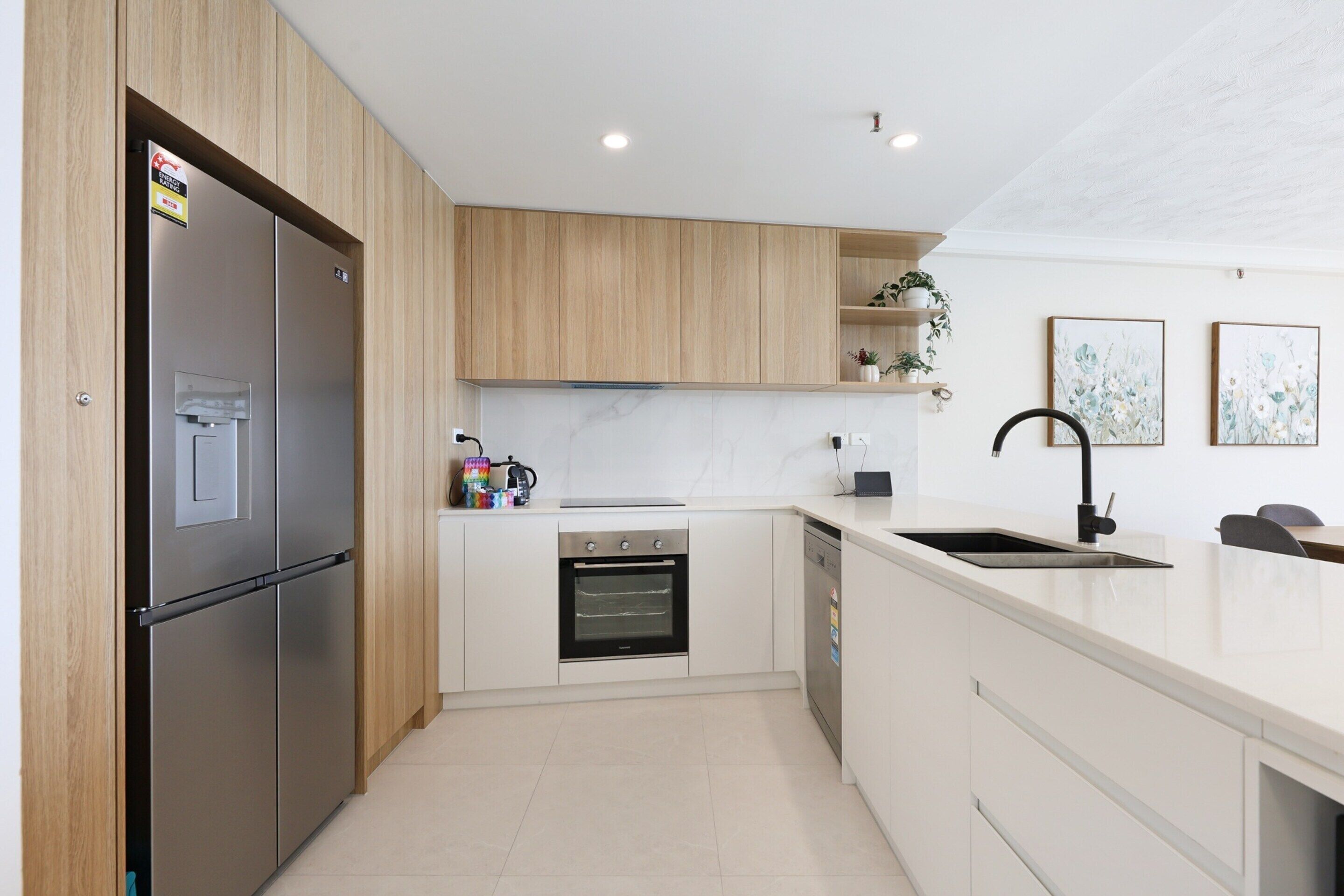 A modern kitchen with wooden cabinets, a stainless steel refrigerator, a built-in oven, and a dishwasher.