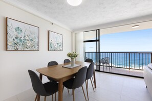 A dining area with a wooden table and chairs, a vase with flowers, and a view of the ocean through a balcony. - Beachfront Stylish Apartment With Ocean Views (Gold Coast)