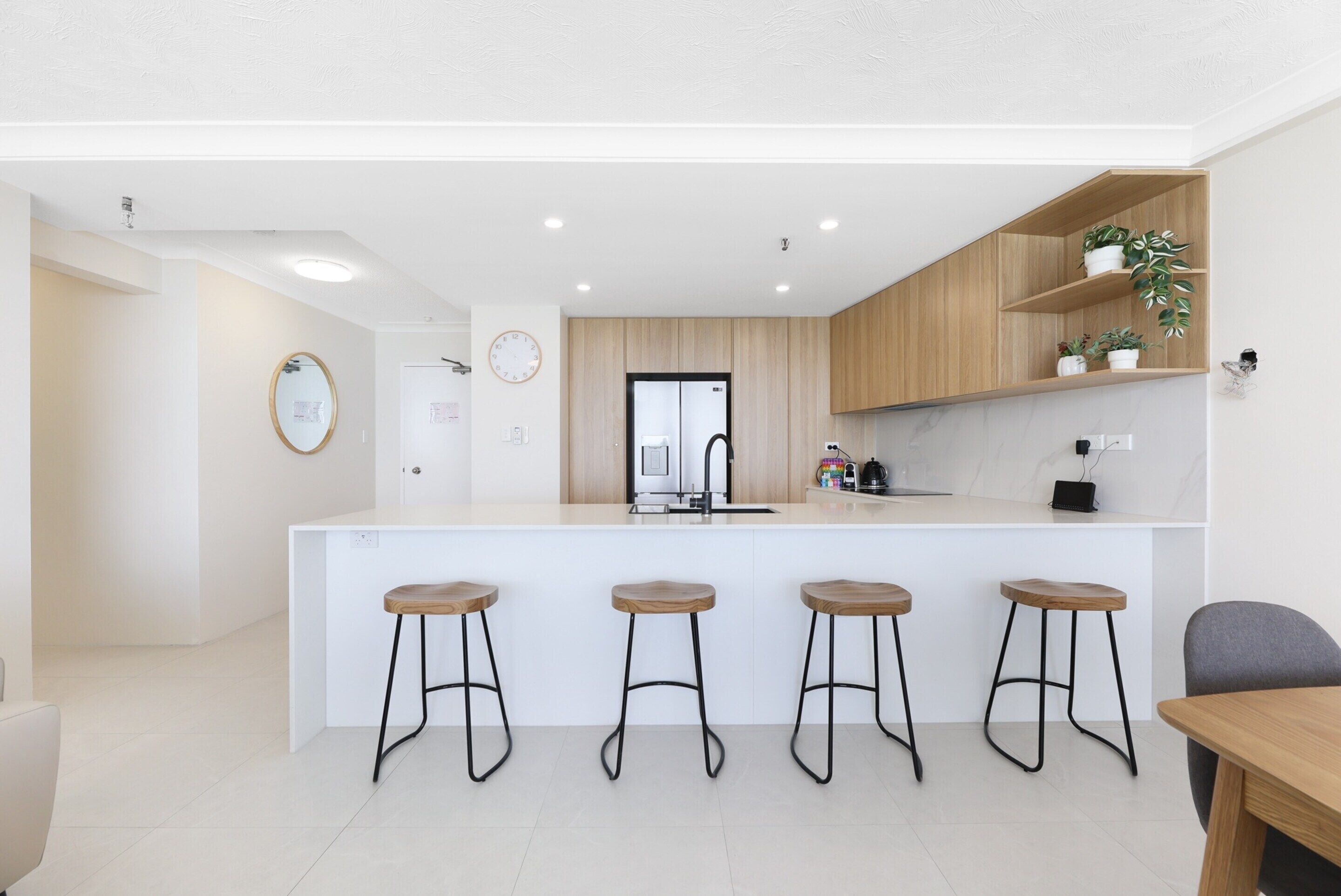 Een moderne keuken met een centraal eiland, houten krukken en inbouwplanken.