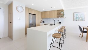 A modern kitchen with a central island, bar stools, a refrigerator, and a clock on the wall.