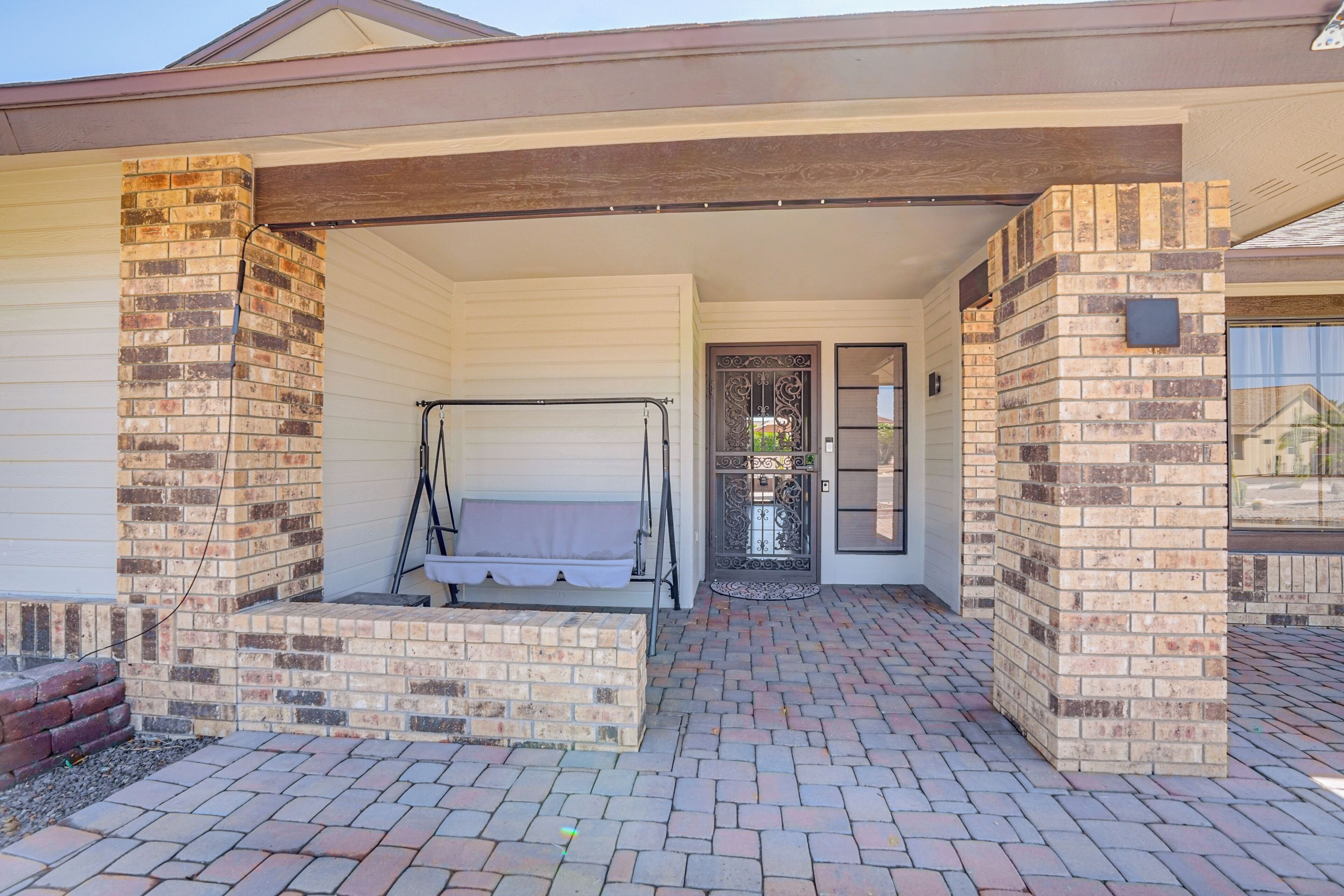 A covered porch with a swing set, brick pillars, and a door with decorative metalwork.