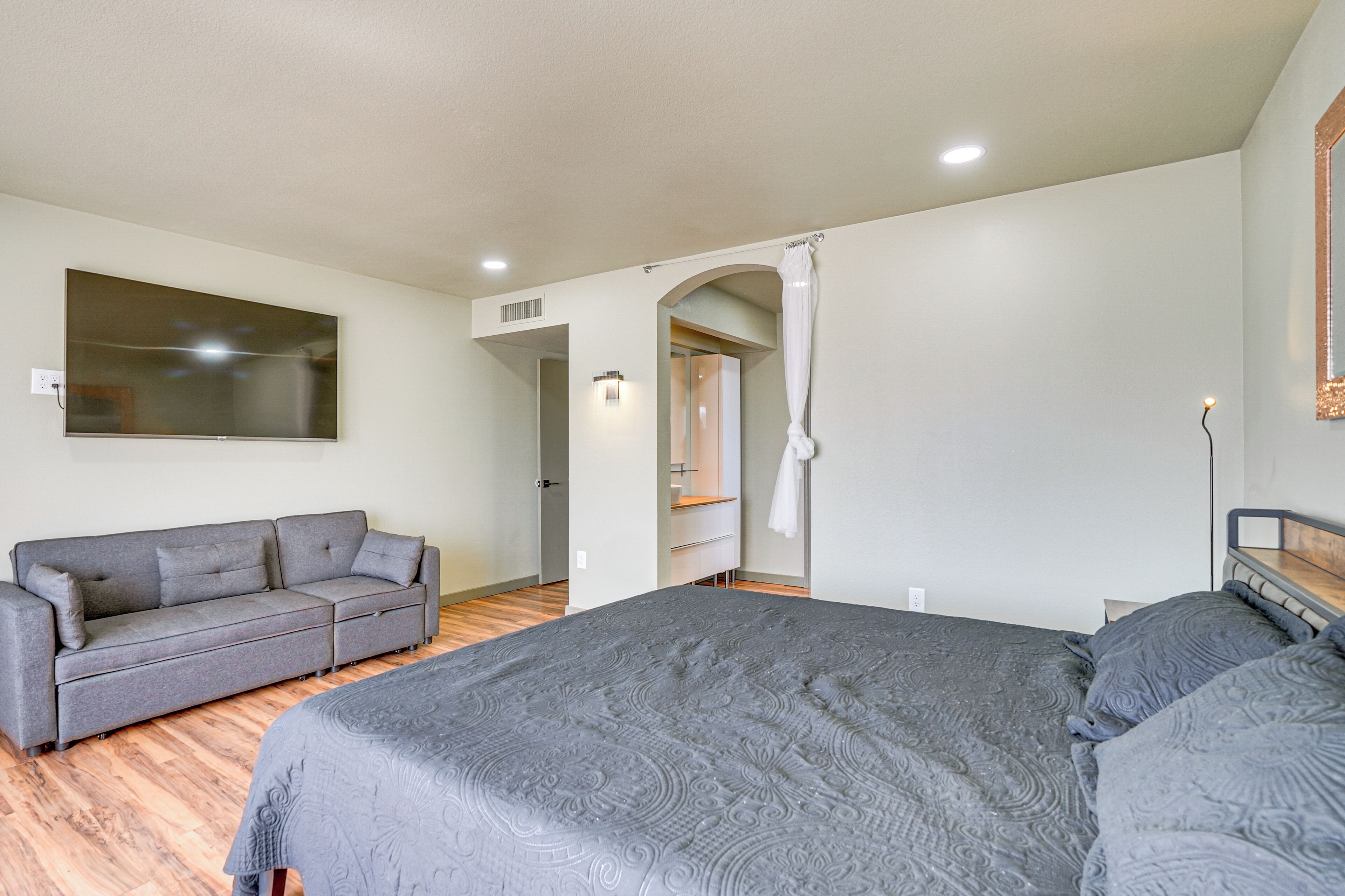 A bedroom with a large bed, a grey sofa, and a mirror on the wall.