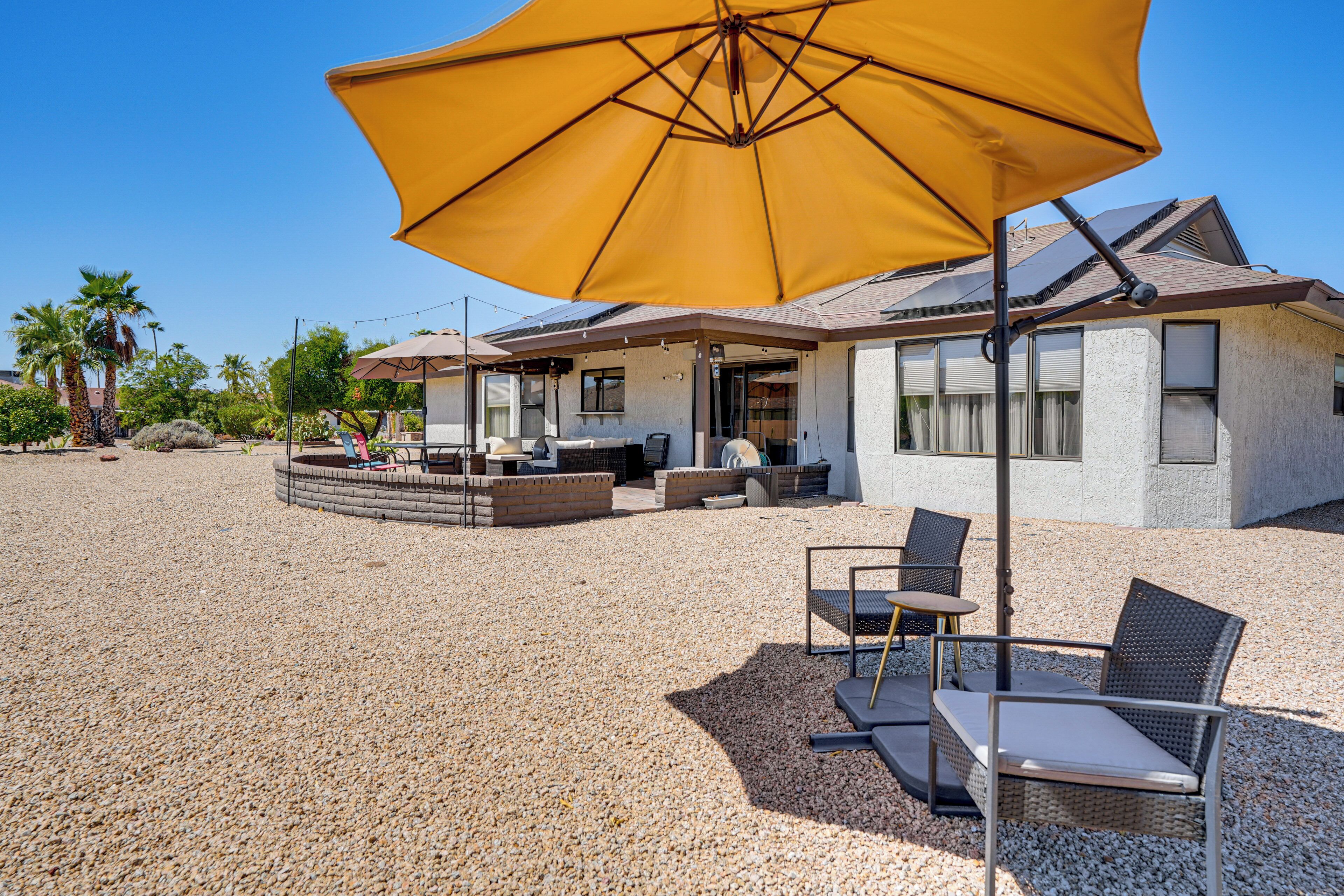 A covered outdoor seating area with a yellow umbrella, a pool, and a house with a sloped roof in the background.
