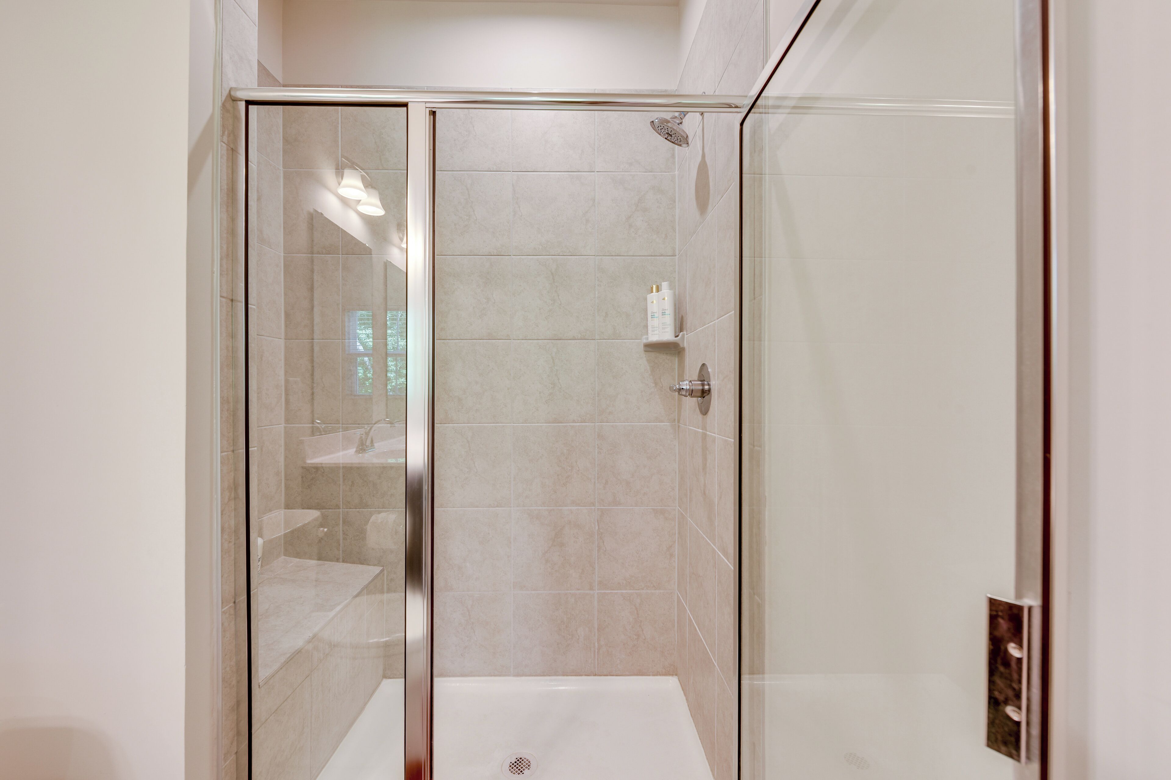 A modern bathroom with a glass-enclosed shower, a white bathtub, and a tiled wall.