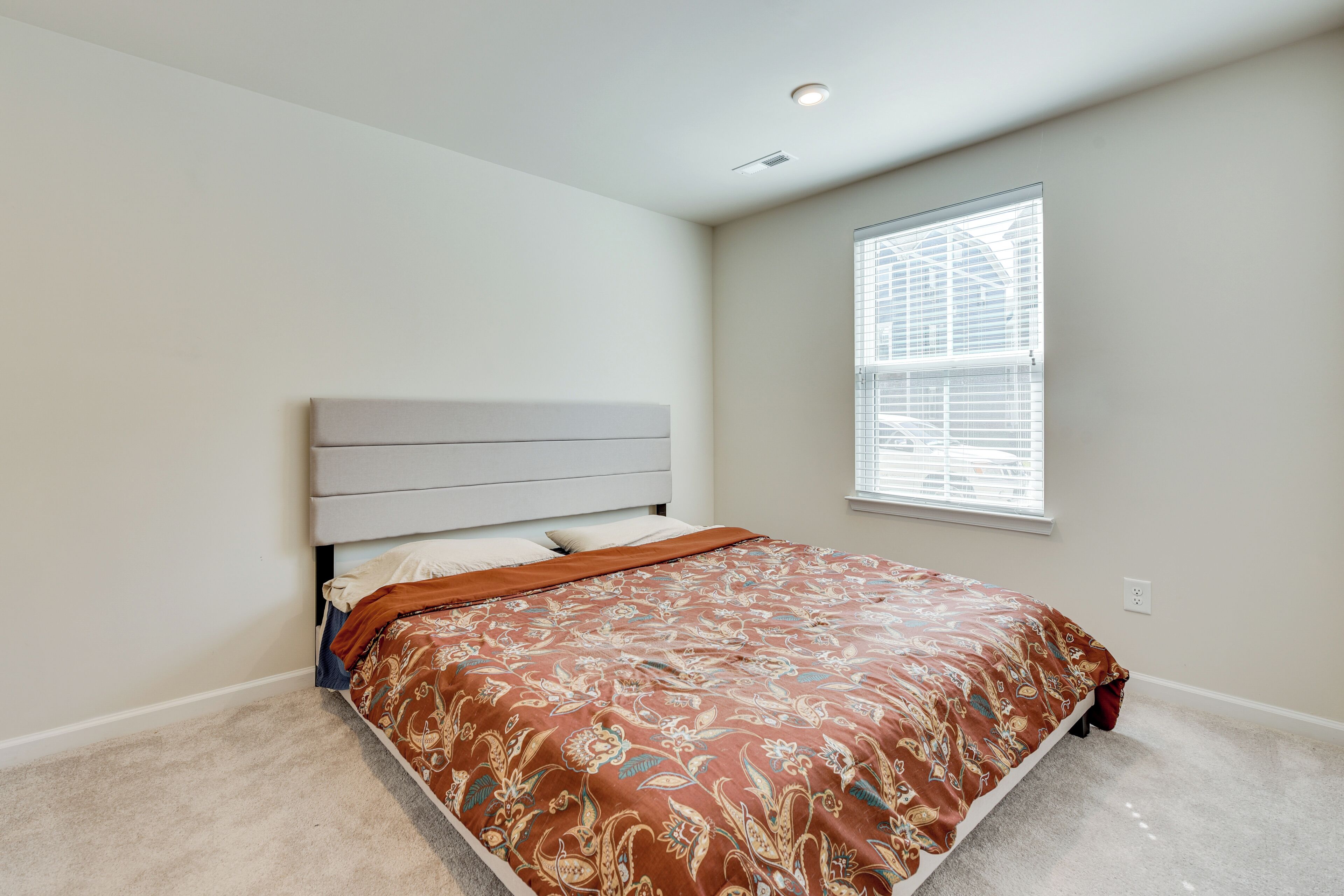 Un dormitorio con cama, ventana con persianas y una lámpara en el techo.