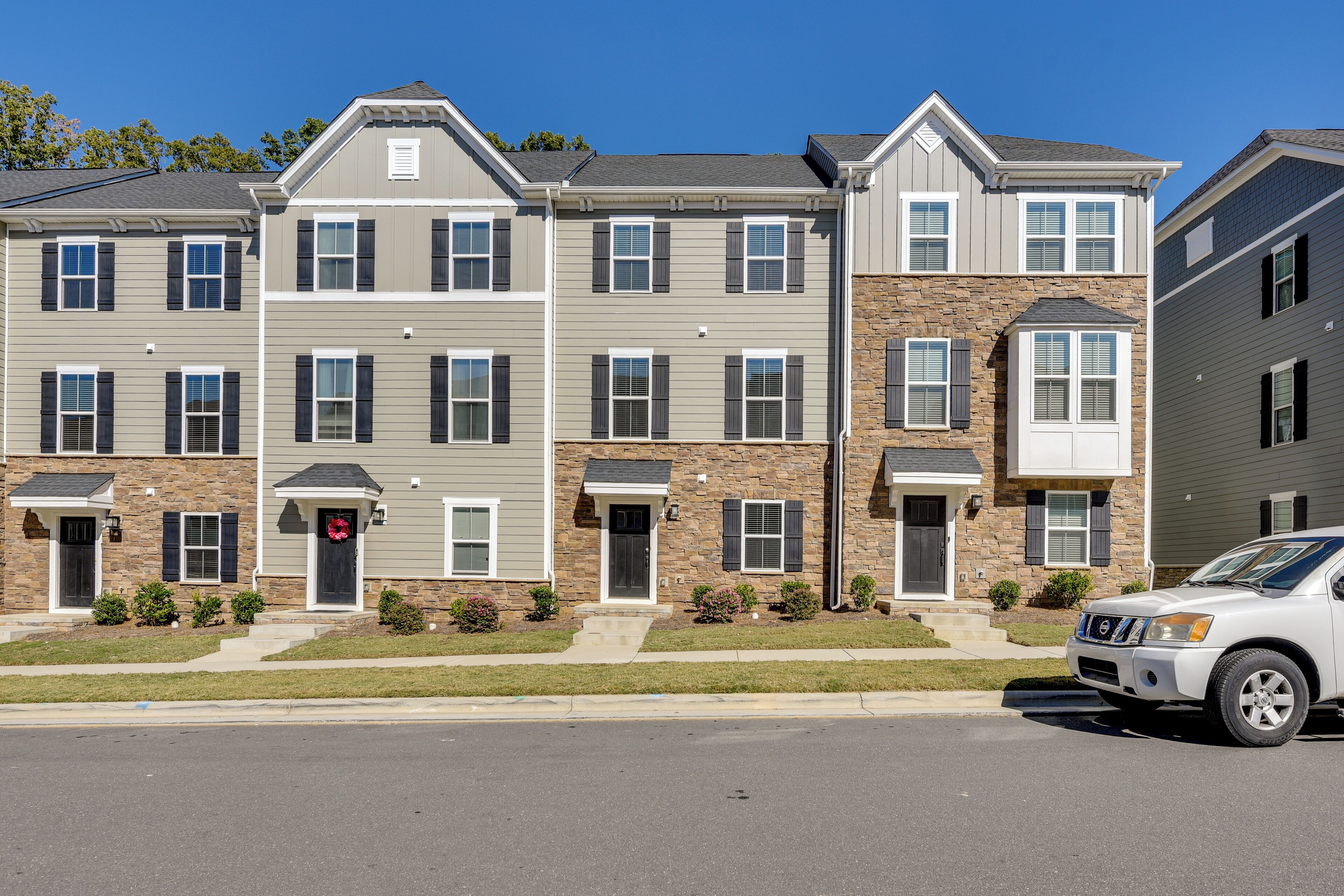 A multi-story residential building with a uniform facade, a central entrance, and a driveway with a parked vehicle.