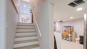Eine Treppe führt zu einem Raum mit einem Fenster, einem Metallregal mit diversen Gegenständen und einem Kühlschrank.