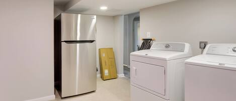 A compact kitchen with a stainless steel refrigerator, a washing machine, and a dryer.