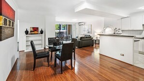 A modern living space with a dining area, a sofa, and a kitchen. - Poolside 2-bed Haven, Walk to City Centre (Sydney)