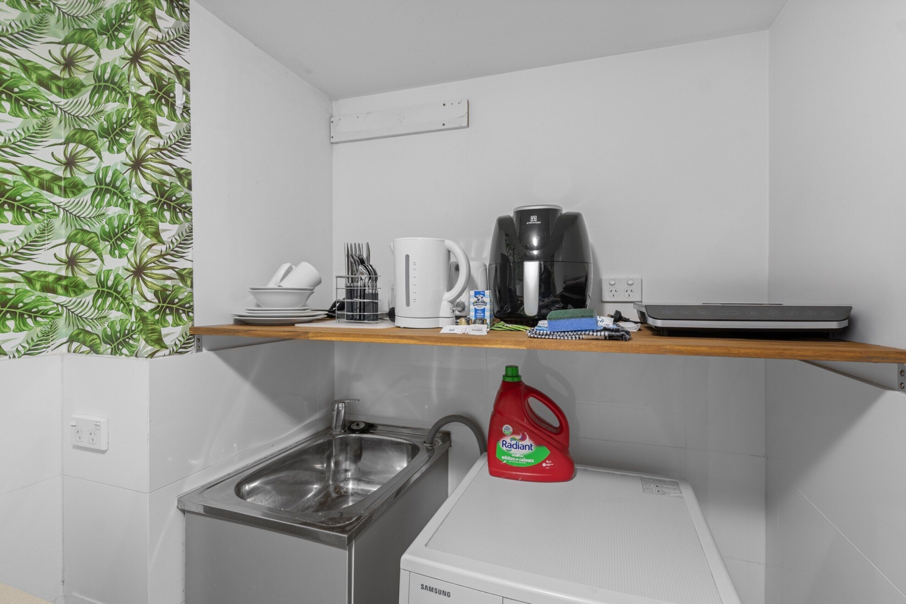 A kitchen with a sink, a coffee maker, a kettle, and a red bottle of detergent.