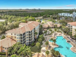 A multi-story hotel with a swimming pool, surrounded by palm trees and a clear view of the surrounding landscape.