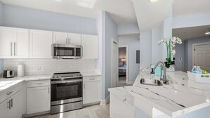 A modern kitchen with white cabinets, stainless steel appliances, and a marble countertop. - Serene Disney Getaway, Designer Style, MP61 (Orlando)