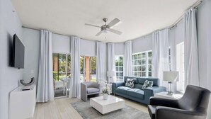 A modern living room with a flat-screen TV, a ceiling fan, a sofa, a coffee table, and a chair. - Serene Disney Getaway, Designer Style, MP61 (Orlando)
