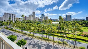 A cityscape with tall buildings, a clear sky, and a road lined with palm trees. - Walkable Urban Retreat! Condo in Honolulu (Honolulu)