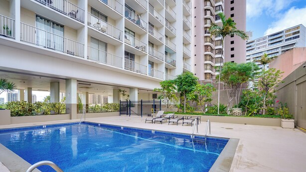 A swimming pool with a metal ladder, surrounded by a concrete deck and lounge chairs. - Walkable Urban Retreat! Condo in Honolulu (Honolulu)
