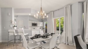 A modern dining area with a chandelier, white chairs, and a table set for four. - Sleek & Stylish Stay, Mins to Magic, MP68 (Orlando)