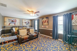 A room with a ceiling fan, a large couch with decorative pillows, a patterned carpet, and artwork on the walls. - Championsgate Resort Perks! Fun-filled Family Home (Davenport)