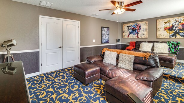 A living room with a brown leather sofa, ottoman, and a ceiling fan. - Championsgate Resort Perks! Fun-filled Family Home (Davenport)