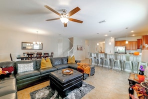 A modern living room with a sectional sofa, a ceiling fan, and a dining area with a bar. - Championsgate Resort Perks! Fun-filled Family Home (Davenport)
