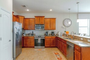 Una cocina con armarios de madera, electrodomésticos de acero inoxidable, un reloj en la pared y una calabaza decorativa en la encimera.