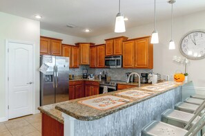 A kitchen with wooden cabinets, stainless steel appliances, a granite countertop, and a clock on the wall.