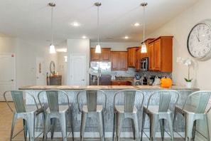 A kitchen with a central island, bar stools, wooden cabinets, stainless steel appliances, and a large wall clock. - Championsgate Resort Perks! Fun-filled Family Home (Davenport)