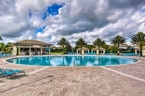 A swimming pool with lounge chairs and a covered area, surrounded by palm trees and buildings.