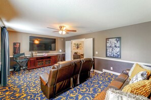 A living room with a large flat-screen TV, leather recliner chairs, a ceiling fan, and a patterned carpet. - Championsgate Resort Perks! Fun-filled Family Home (Davenport)