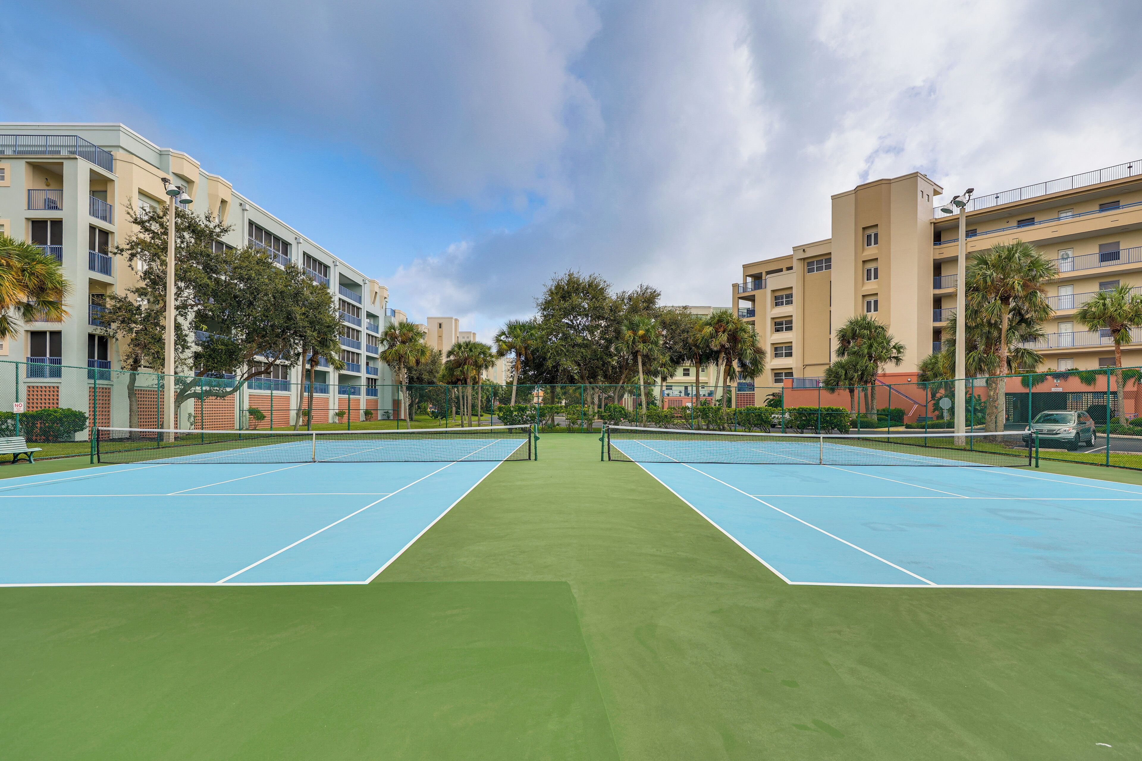 Een tennisbaan met een net, omgeven door gebouwen en palmbomen.